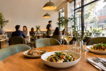Warm modern restaurant dining room with fresh dishes, wood tables, and soft natural daylight indoors