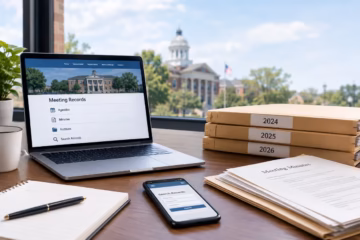 Municipal meeting minutes, archived records, and year-labeled folders on a desk near City Hall.