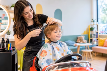 A smiling child gets a gentle haircut from a stylist in a welcoming children's salon nearby indoors.