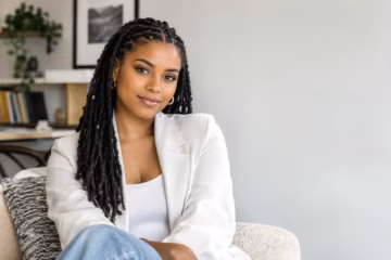 Cieana Monae smiling in a modern room while wearing a white blazer and braided hair.
